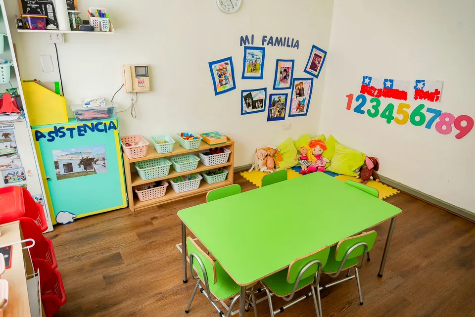 Sala de Nanai con mesas verdes, panel de asistencia y rincón de juego